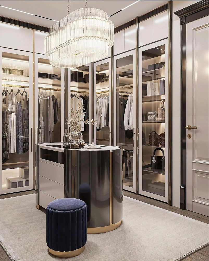 High-end boutique dressing room with glass wardrobe doors, chandelier, and custom storage island by Los Angeles Closet in Los Angeles CA